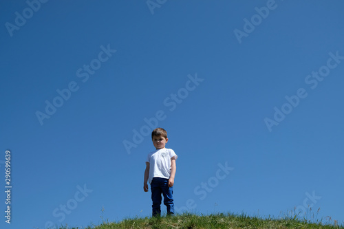 Trauriger, einsamer Junge auf einer Bergkuppe mit blauem Himmerl im Hintergrund