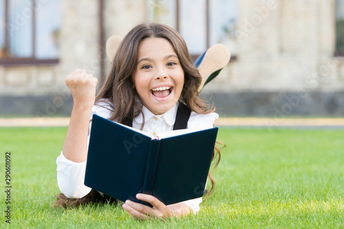 Studying concept. Schoolgirl school uniform laying on lawn with favorite book. Extracurricular reading. Cute small child reading book outdoors. Basic education. Adorable little girl learn reading