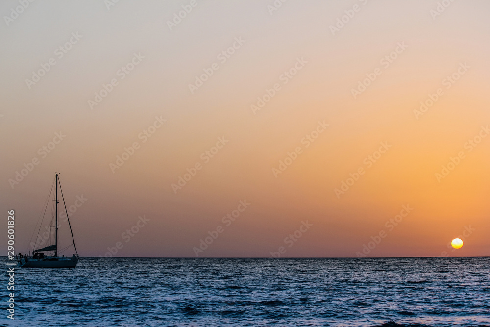 a sailboat and the sun against light during sunset at the beach of caletta on the island of San Pietro in Sardinia