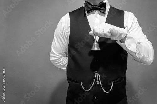 Black and White Portrait of Butler in White Gloves and Vest Holding a Bell. Concept of Service Industry and Professional Hospitality. Dependable Servant. Copy Space for Service.