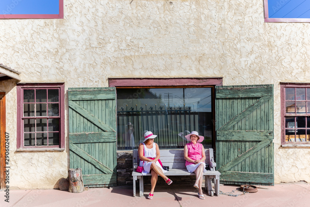 two women sitting on an old bench in front of an abandoned  store