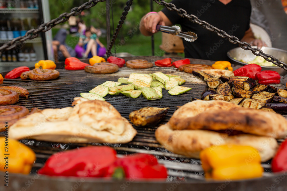 A large round grill on the coals in which grilled color vegetables and fresh meat sausages are cooked. Food and equipment for cooking at a food festival