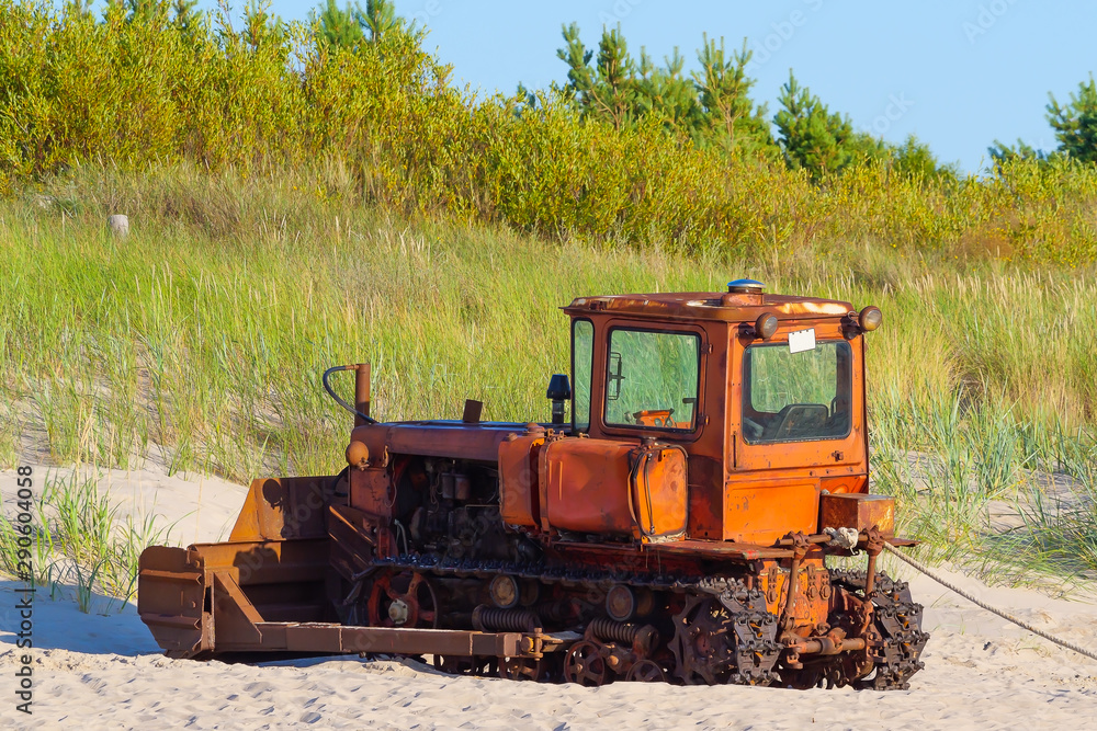 An old caterpillar tractor stands on a sandy shore. An old caterpillar tractor stands on a sandy shore.