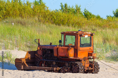 An old caterpillar tractor stands on a sandy shore. © Igor