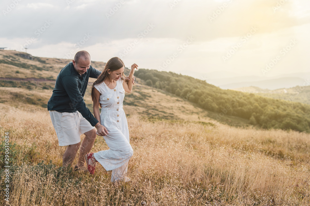 Young couple man and woman in love walking on the field on the mountain in autumn or summer day hugging together having fun bonding flirting flirt husband and wife lovers Young couple man and woman in love walking on the field on the mountain in autumn or summer day hugging together having fun bonding flirting flirt husband and wife lovers