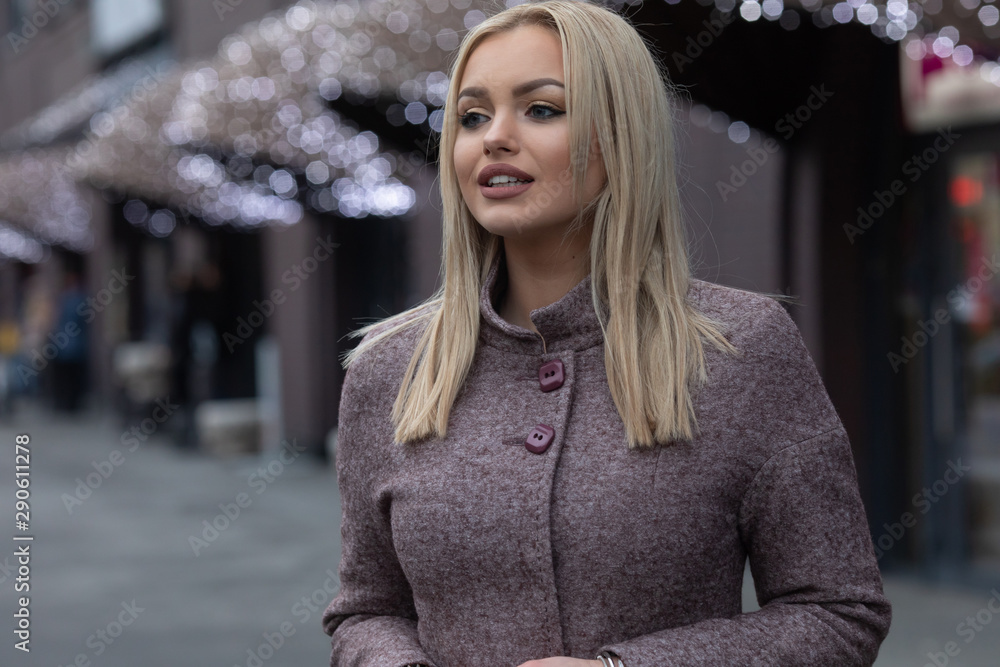 Beautiful blonde girl in a city. Stylish woman in a coat. Smiling. 