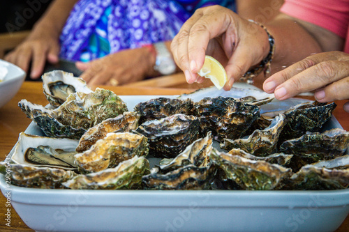 Woman,s hand squeezing a slice of lemon on a big plateau of raw oysters