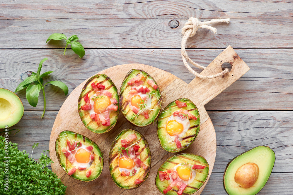Top view on grilled avocado boats with bacon and quail eggs, flat lay on wood Top view on grilled avocado boats with bacon and quail eggs, flat lay on wood