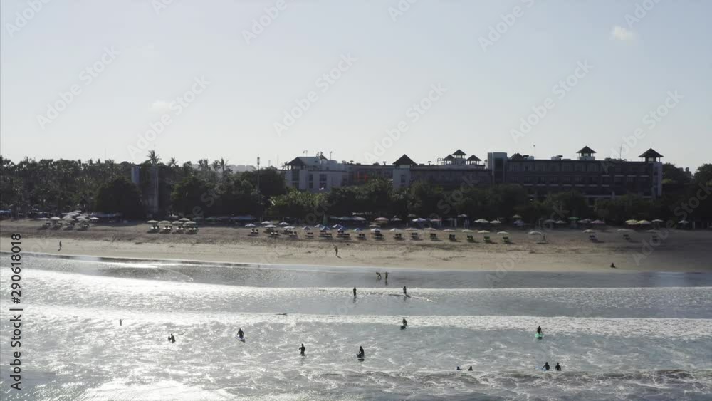 Aerial view of tourists learning how to surf ocean waves at morning Kuta spot, the safiest spot in Bali, Indonesia. Resort and hotel are on the background Aerial view of tourists learning how to surf ocean waves at morning Kuta spot, the safiest spot in Bali, Indonesia. Resort and hotel are on the background
