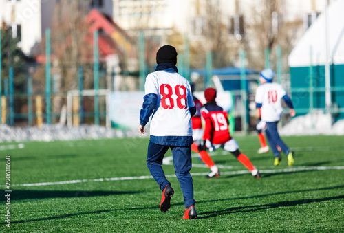 Boys in white and red sportswear plays football on field, dribbles ball. Young soccer players with ball on green grass. Training, football, active lifestyle for kids , winter sport
