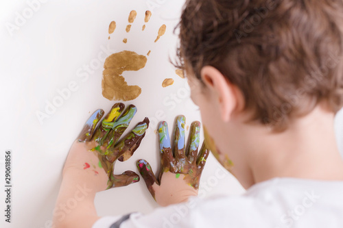 Boy with his hands full of finger paint, painting the white wall with his hands. Little Artist.