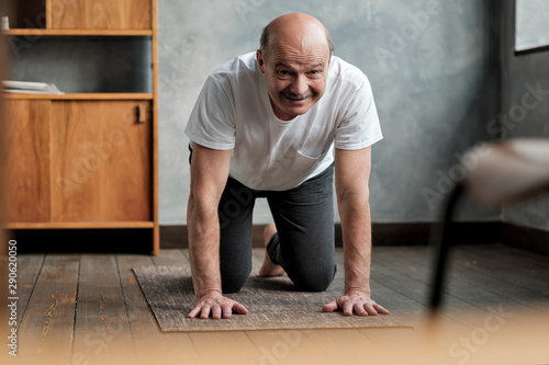 Senior hispanic man practices yoga asana marjariasana or cat-cow pose at home. Doing sport exercise for spine health. photo