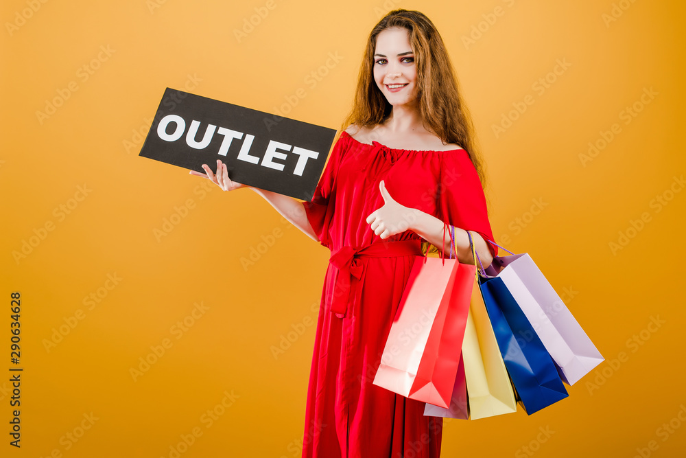 smiling young woman with thumbs up has outlet sign with colorful shopping bags isolated over yellow smiling young woman with thumbs up has outlet sign with colorful shopping bags isolated over yellow