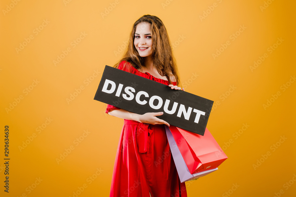 smiling pretty girl has discount sign with colorful shopping bags isolated over yellow smiling pretty girl has discount sign with colorful shopping bags isolated over yellow