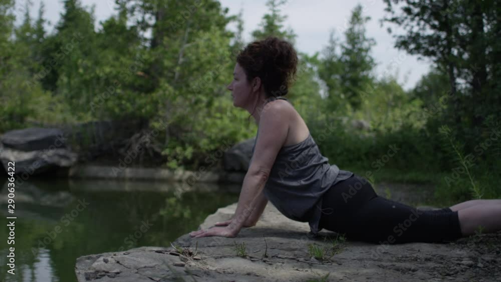 Middle aged woman practicing yoga relaxation on the shore of a lake
