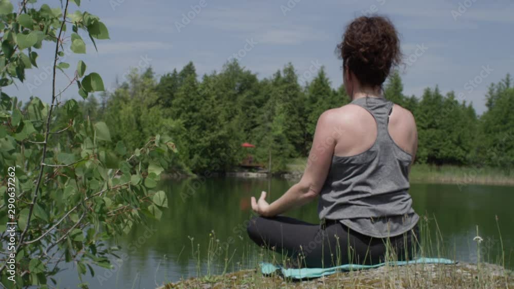 Middle aged woman practicing yoga relaxation on the shore of a lake Middle aged woman practicing yoga relaxation on the shore of a lake