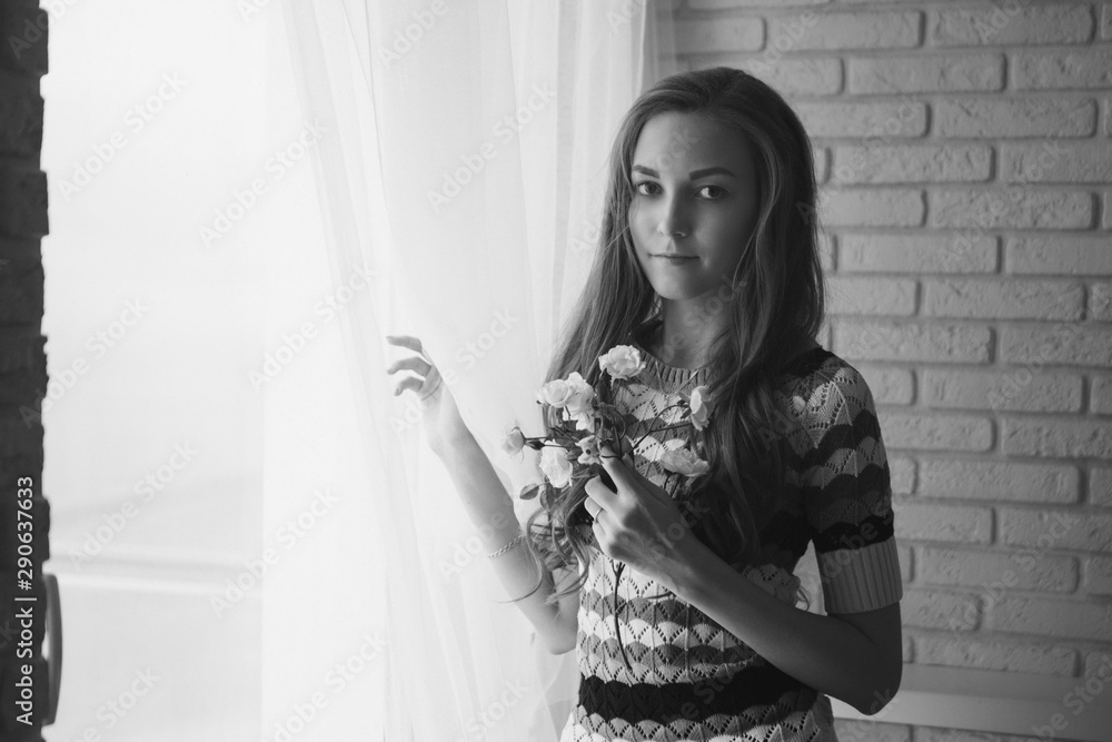 A beautiful girl without makeup with flowers looks out from behind the curtain, a woman at the window. The concept of advertising natural makeup, morning pastime A beautiful girl without makeup with flowers looks out from behind the curtain, a woman at the window. The concept of advertising natural makeup, morning pastime