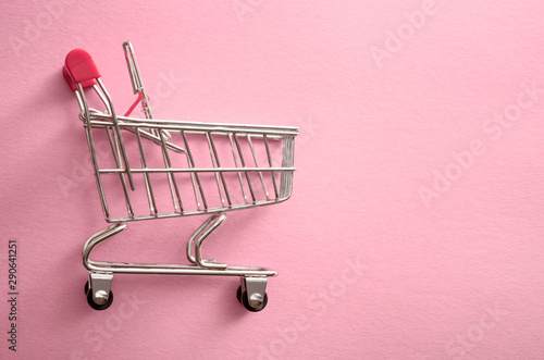 Empty shopping cart over pink background. Flat lay, top view