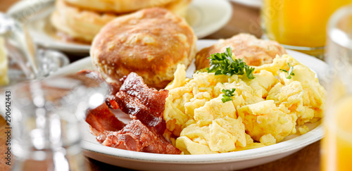 huge breakfast plate with scrambled eggs, bacon and biscuits
