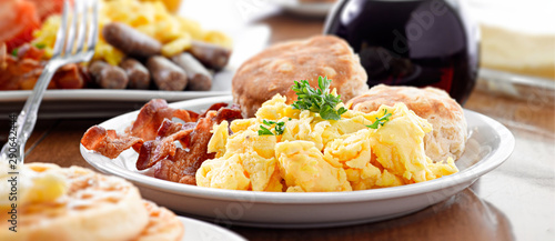 huge breakfast plate with scrambled eggs, bacon and biscuits