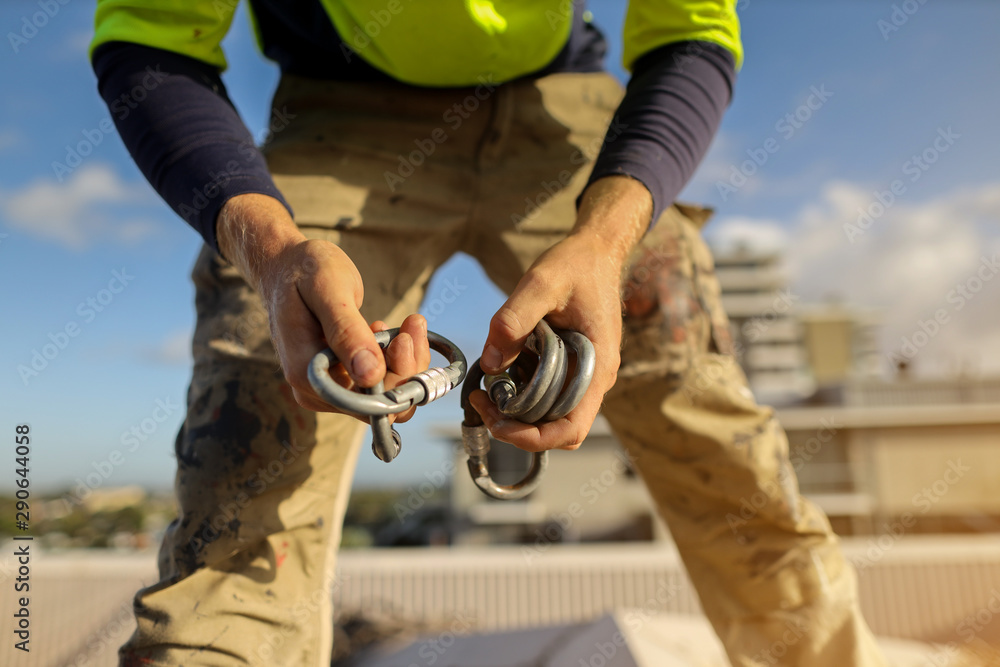 Rope access worker conducting safety inspecting of hard wear screwgate locking carabiners on his hand before connecting onto abseiling fall arrest fall restraint roof anchor point prior to use on site Rope access worker conducting safety inspecting of hard wear screwgate locking carabiners on his hand before connecting onto abseiling fall arrest fall restraint roof anchor point prior to use on site