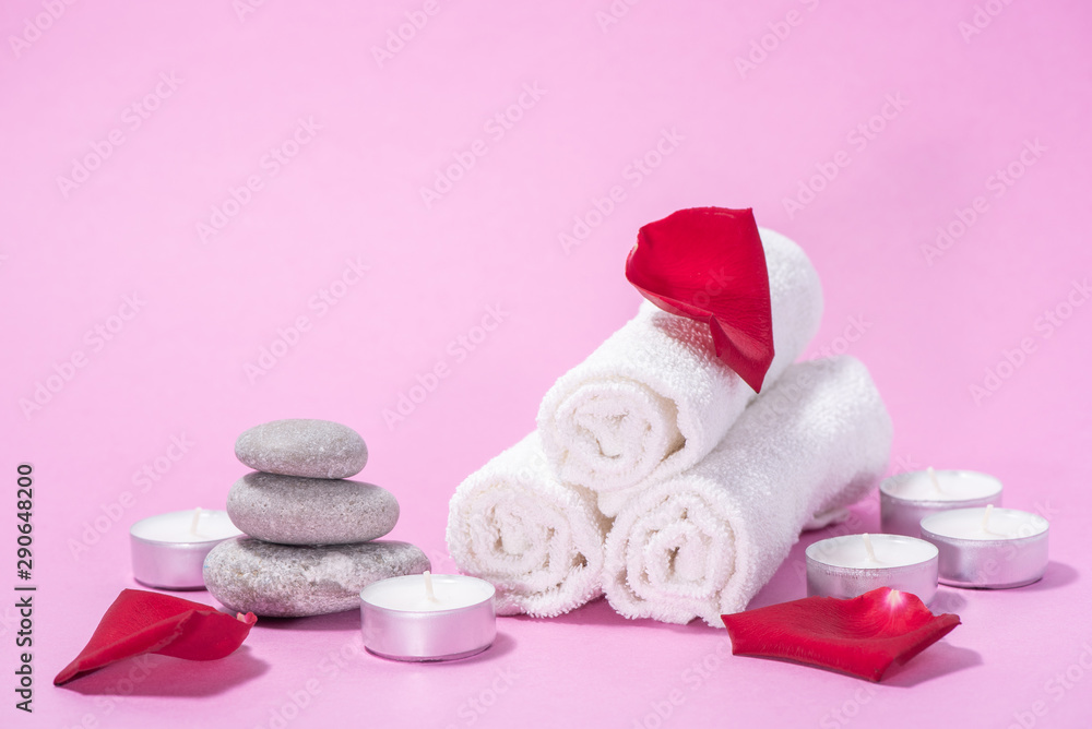 White soft towels, red rose, stones and candles for skin care and spa on a pink background