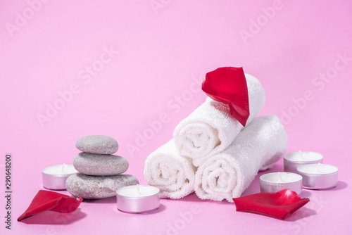 White soft towels, red rose, stones and candles for skin care and spa on a pink background