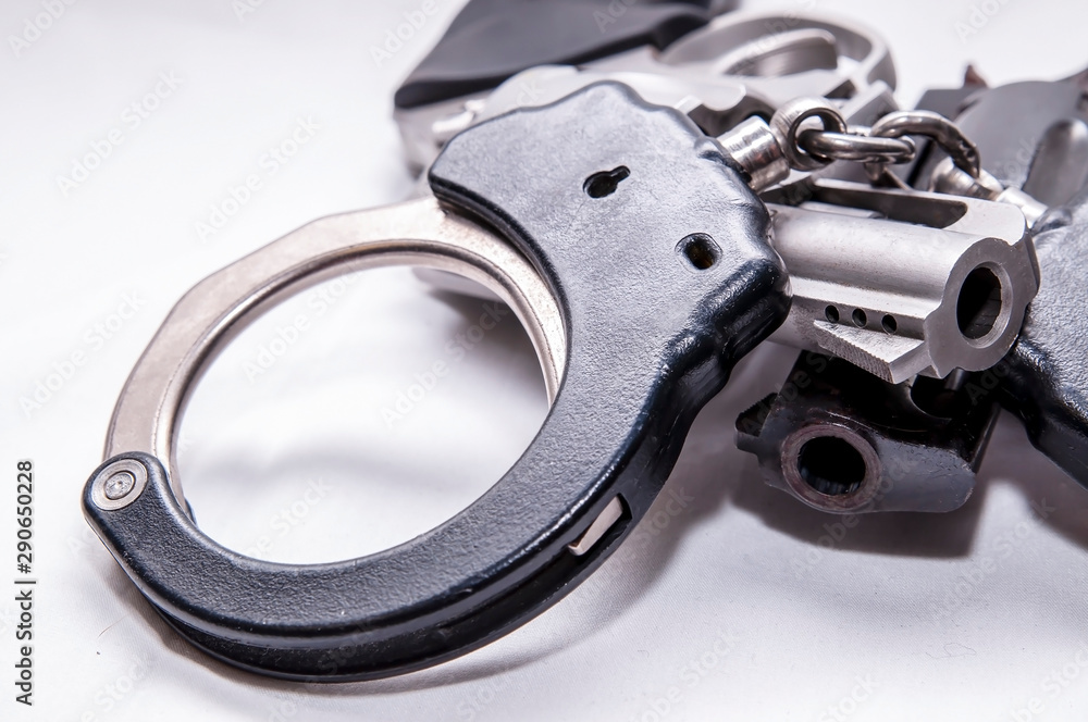 A set of two toned metal handcuffs on top of two revolvers, one black and the other stainless on a white background A set of two toned metal handcuffs on top of two revolvers, one black and the other stainless on a white background