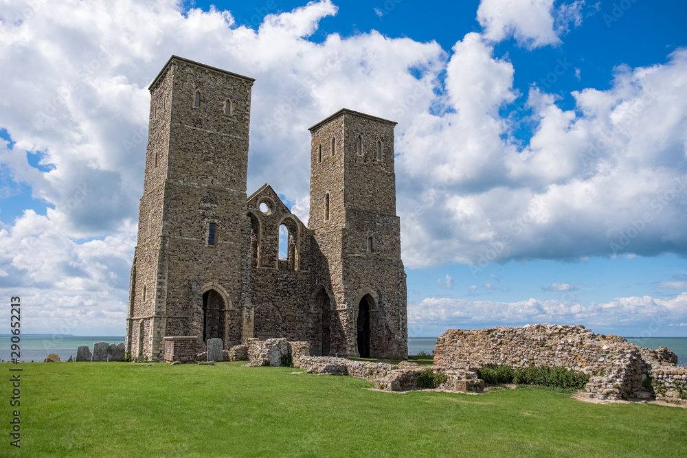 An old ruin of a church now lays on the coastline, with just two towers still standing overlooking the sea, on a partially cloudy day in England, UK.