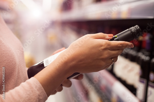 A woman takes alcoholic drinks from the supermarket shelf. Shopping for alcohol in the store.
