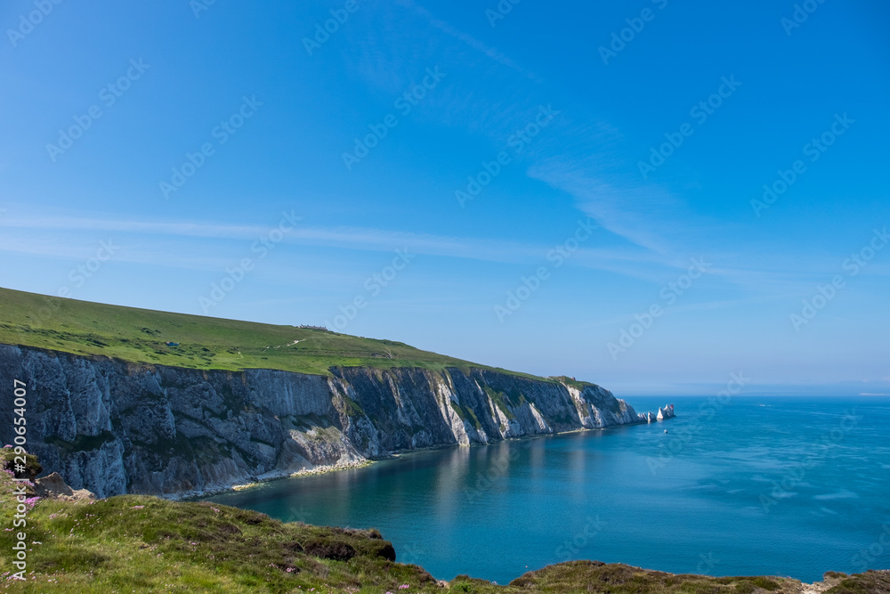 The crisp white chalk cliffs covered in a layer of bright green vegetation overlooking the sea on a clear and sunny day on the Isle of Wight.