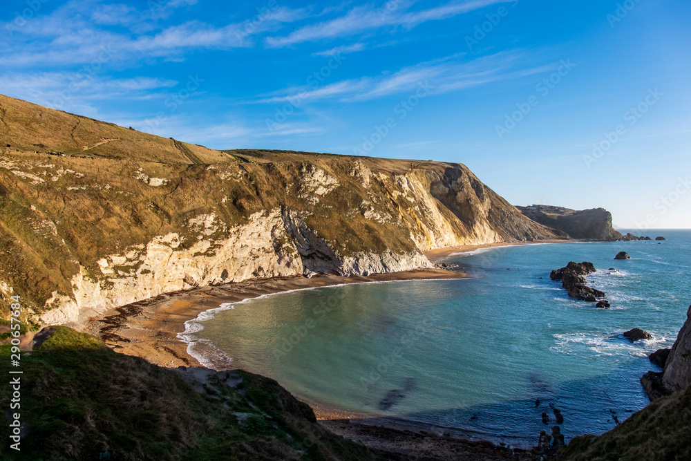 Two curved beaches are nestled against the hills overlooking the sea with a few rock formations near this cove on a clear and sunny day in England, UK.