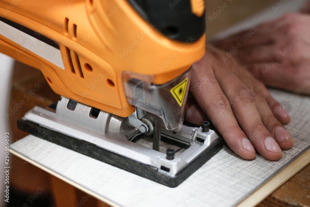 Yellow electric jigsaw sawing laminate. Close up