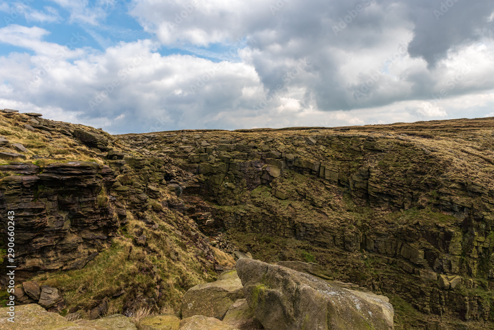 The rocky hills of the Peak District are covered in yellow vegetation on a partially cloudy day in England, UK.