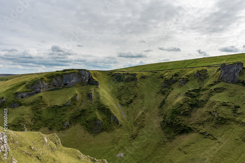 Looking up to alien-like rocky hills covered in a green moss and grass on partially cloudy day in England, UK.