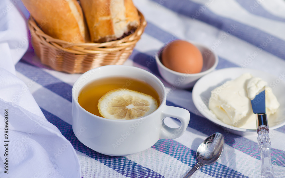 Breakfast on the grass. Green tea with lemon, bread with butter and egg for the traditional breakfast. French breakfast in the open air. Breakfast on the grass. Green tea with lemon, bread with butter and egg for the traditional breakfast. French breakfast in the open air.