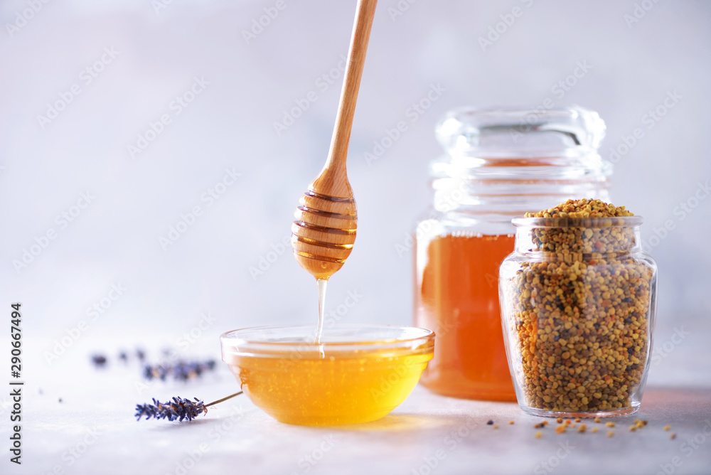 Bee pollen granules, honey jar with wooden dropper, honeycomb on grey backdrop. Copy space. Autumn harvest concept Bee pollen granules, honey jar with wooden dropper, honeycomb on grey backdrop. Copy space. Autumn harvest concept