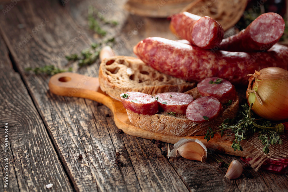 Dry-cured sausage with bread and spices on a old wooden table.