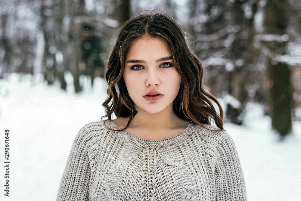 Outdoor close up portrait of young beautiful teenage girl with long hair wearing sweater posing in forest. Christmas, winter holidays concept. Snowfall. Outdoor close up portrait of young beautiful teenage girl with long hair wearing sweater posing in forest. Christmas, winter holidays concept. Snowfall.