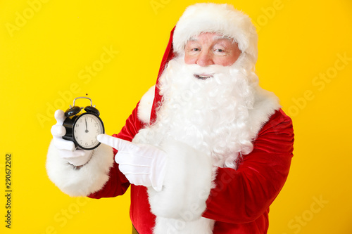 Santa Claus with alarm clock on color background