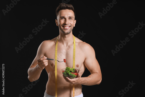 Handsome muscular man with measuring tape and salad on dark background. Weight loss concept