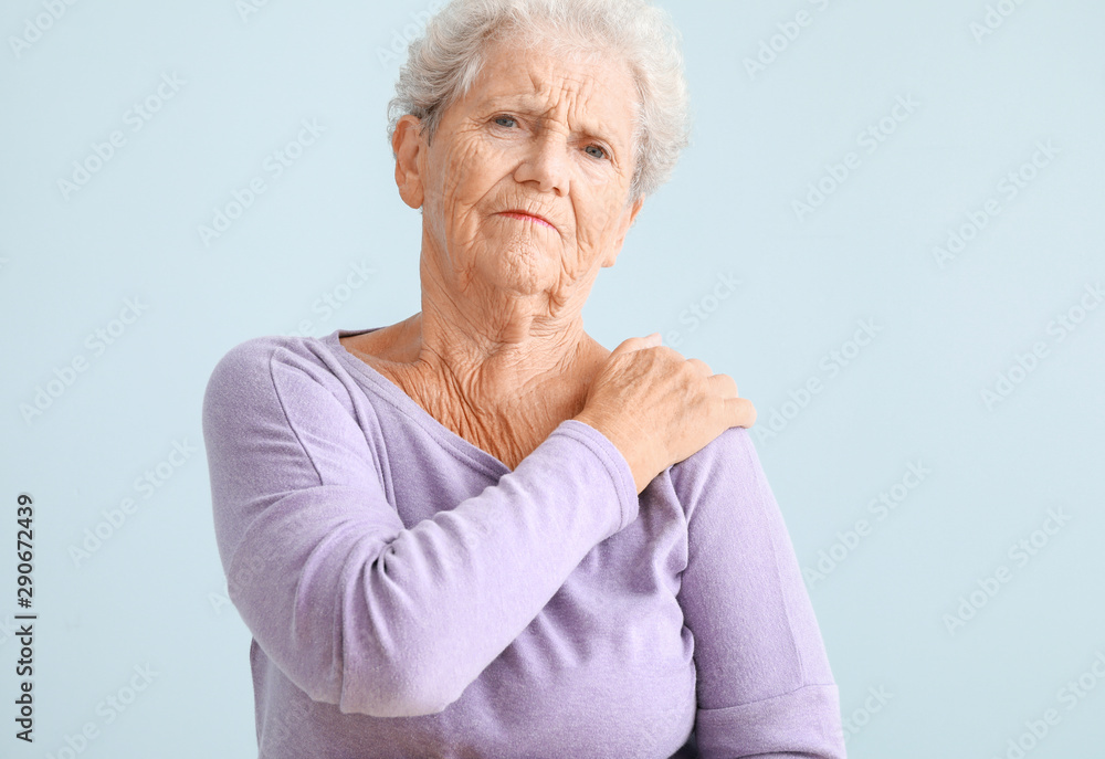 Senior woman suffering from pain in shoulder against light background Senior woman suffering from pain in shoulder against light background