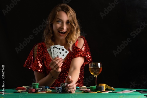 Girl in evening red dress plays poker. Gaming business in a casino or night club. On a black background for design, with smoke.