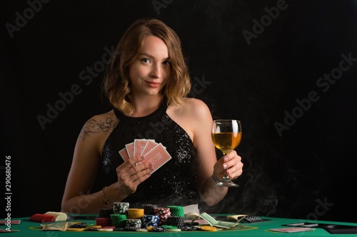 A young girl in a black evening dress plays poker in a casino. Game business and success on a black background with smoke, horizontal photo