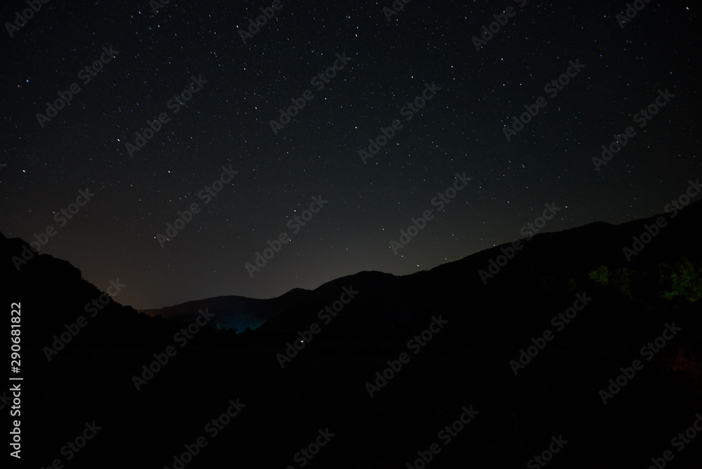 Night starry sky over the mountains. Stars and constellations are visible through light clouds. Night starry sky over the mountains. Stars and constellations are visible through light clouds.