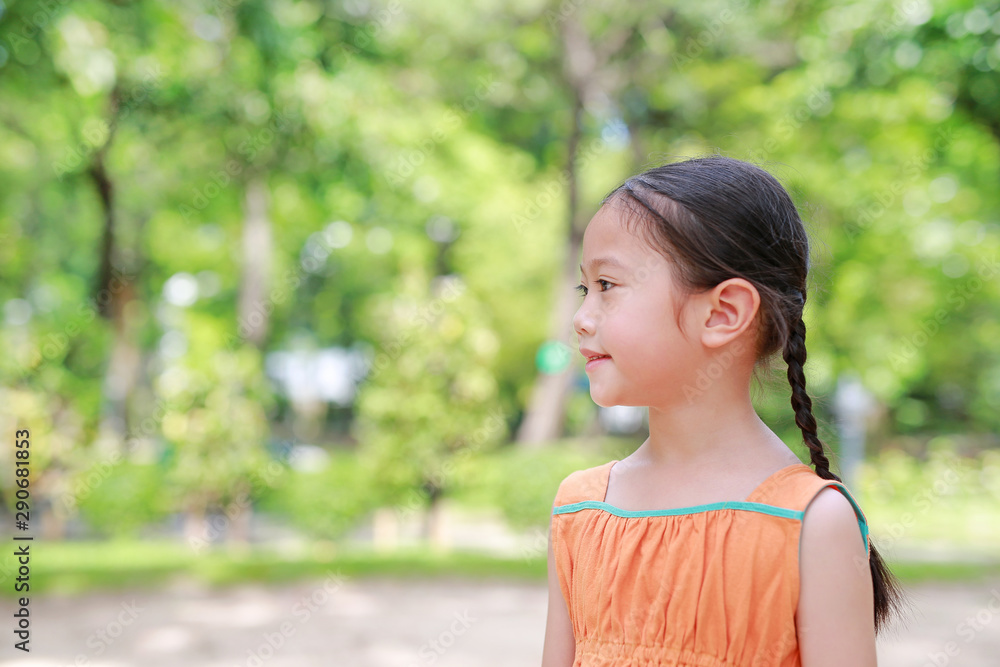 Smiling young little Asian child girl in the green garden. Close-up kid side view portrait. Smiling young little Asian child girl in the green garden. Close-up kid side view portrait.
