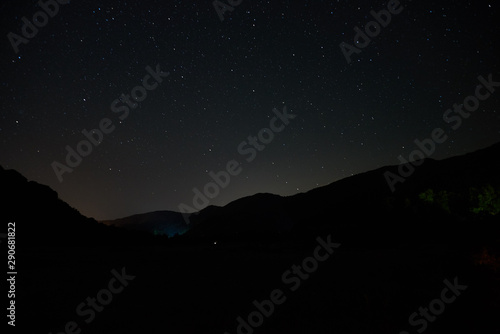 Night starry sky over the mountains. Stars and constellations are visible through light clouds.