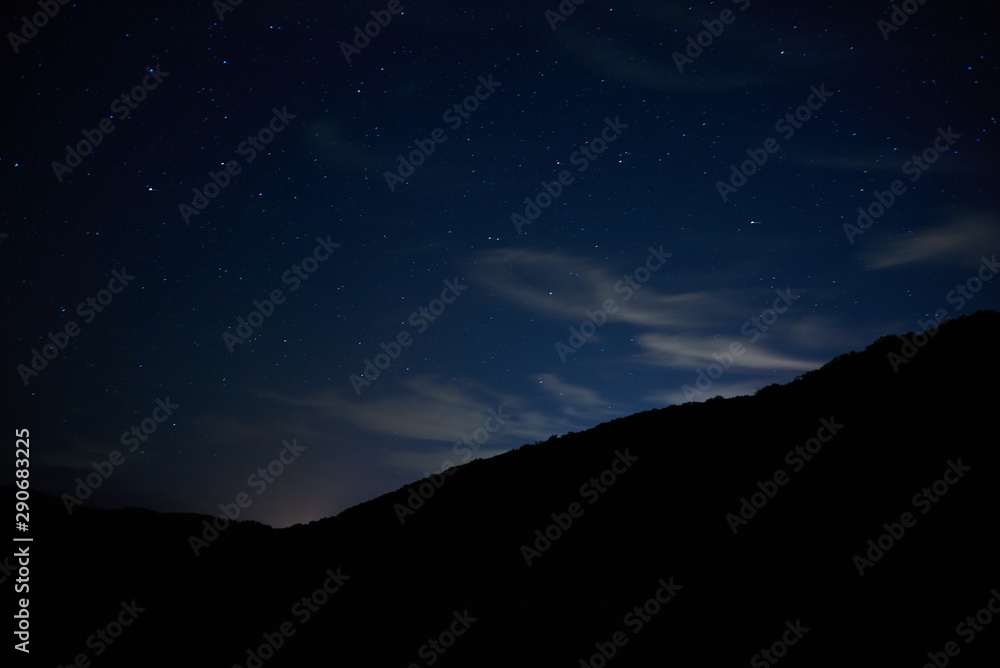 Night starry sky over the mountains. Bright stars and constellations are visible through light clouds. Night starry sky over the mountains. Bright stars and constellations are visible through light clouds.