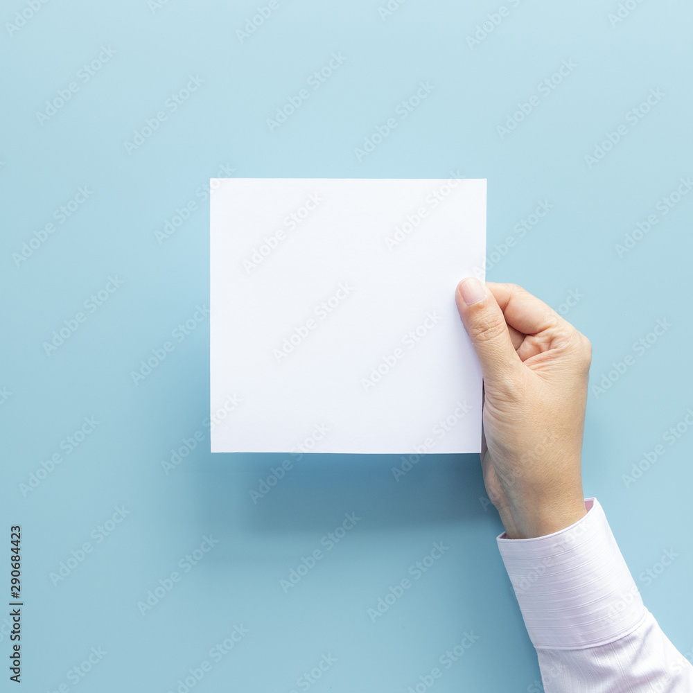 Fototapeta premium woman hand holding blank paper sheet isolated on blue background with copy space.