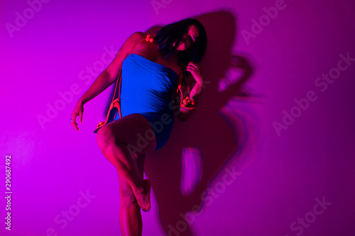 Beautiful black African woman in a blue dress and red high heels on a pink background.